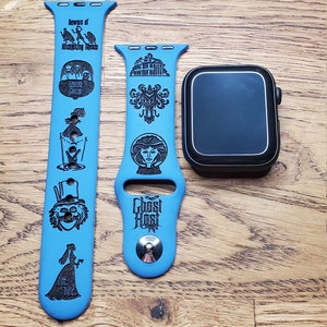 May include: Two blue Apple Watch bands with black engravings of the Haunted Mansion attraction at Disneyland. The band on the left has the text "Beware of Hitchhiking Ghosts" and images of the ghosts. The band on the right has the text "Ghost Host" and images of the mansion and a ghost.