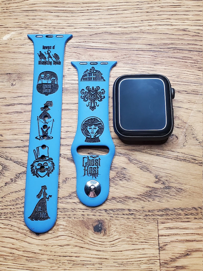 May include: Two blue Apple Watch bands with black engravings of the Haunted Mansion attraction at Disneyland. The band on the left has the text "Beware of Hitchhiking Ghosts" and images of the ghosts. The band on the right has the text "Ghost Host" and images of the mansion and a ghost.