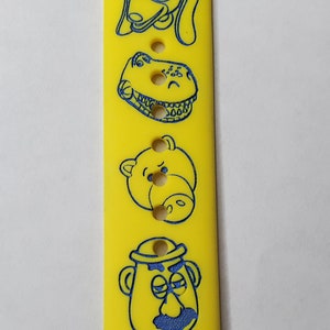 May include: Yellow silicone watch band with blue Toy Story characters including Slinky Dog, Rex, Hamm, and the alien. The band has the text "TOY STORY" printed on it.