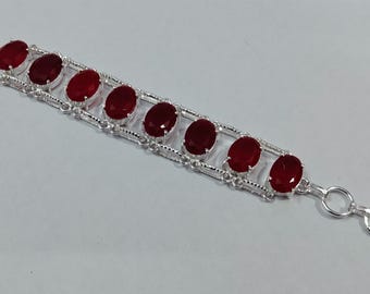 Puede incluir: Un brazalete de plata con un diseño de cadena y piedras preciosas ovaladas rojas.