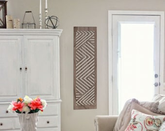 May include: A living room scene featuring a white cabinet, a dark brown coffee table, and a beige sofa with decorative pillows. A tall white vase holds colorful flowers. A wooden wall art piece with a geometric design hangs on the wall.