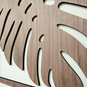 May include: A set of three wooden wall decor pieces featuring a stylized monstera leaf design. The leaves are cut out of the wood and have a dark brown stain.