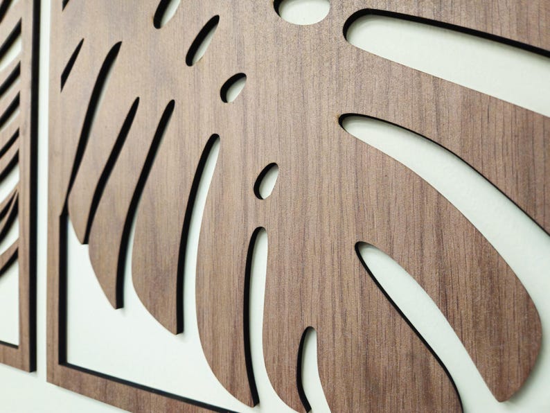 May include: A set of three wooden wall decor pieces featuring a stylized monstera leaf design. The leaves are cut out of the wood and have a dark brown stain.