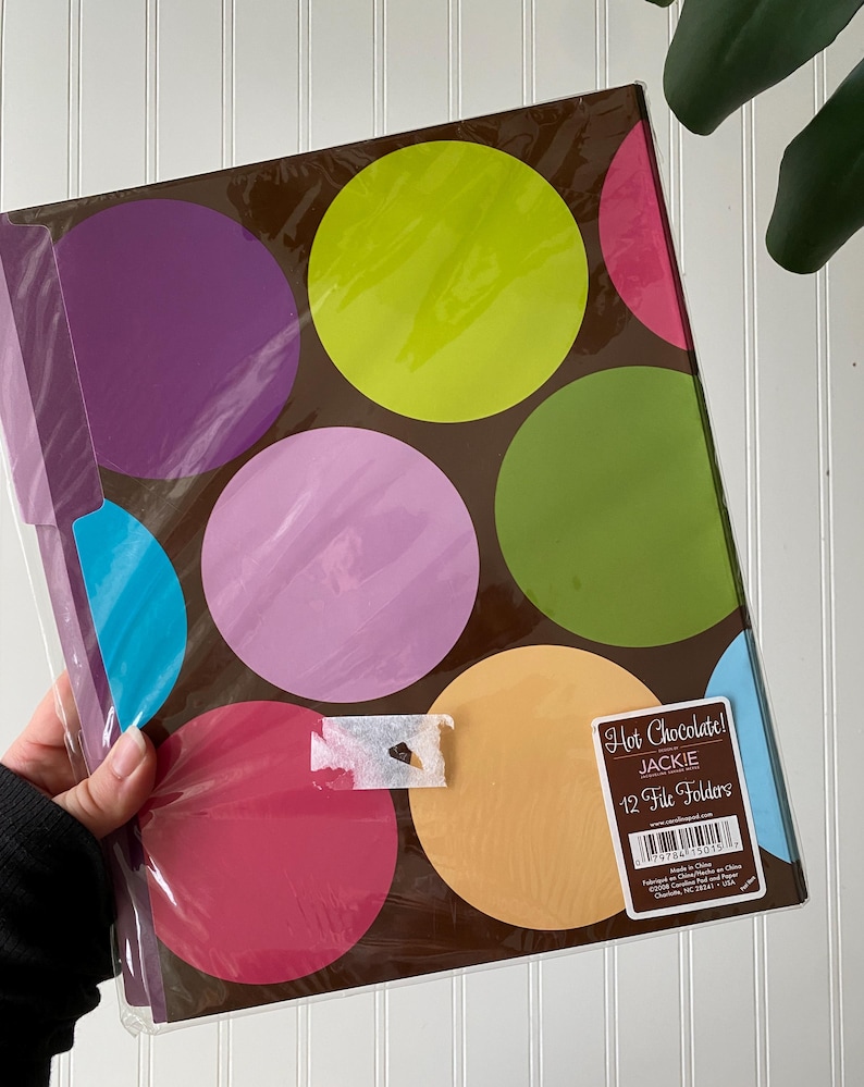 May include: A pack of 12 file folders in a brown base color featuring large, colorful polka dots in shades of lime green, purple, light pink, dark pink, orange, and blue. A rectangular label on the front reads Hot Chocolate! JACKIE 12 File Folders.