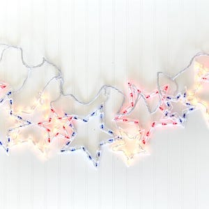 May include: A string of illuminated star-shaped lights in red, white, and blue. The stars are outlined in white and have small lights inside. The string is white and has a plug at the end. Perfect for patriotic holidays.
