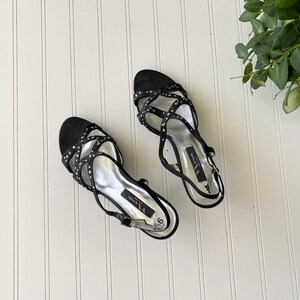 K&ouml;nnte beinhalten: Paar schwarze Sandalen mit Riemchen und silbernen Akzenten. Die Sandalen haben einen Slingback-Riemen und sind mit kleinen silbernen Nieten verziert. Die Sohlen sind silberfarben, und die Schuhe sind Gr&ouml;&szlig;e 9.