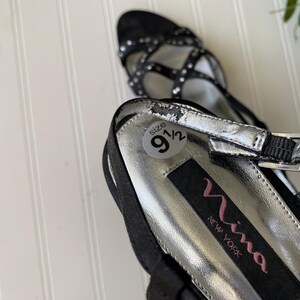 K&ouml;nnte beinhalten: Schwarze Riemchen-High Heels mit silbernen Akzenten und einem Gr&ouml;&szlig;enetikett 9 1/2. Die Schuhe haben eine spitze Zehenpartie und einen Schnallenverschluss. Der Markenname "Nina New York" ist auf der Innensohle sichtbar.