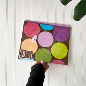 May include: A set of 12 file folders with a brown background featuring large, colorful polka dots in shades of pink, purple, light blue, yellow, and lime green. The packaging includes a label with the text Hot Chocolate Jackie 12 File Folders.