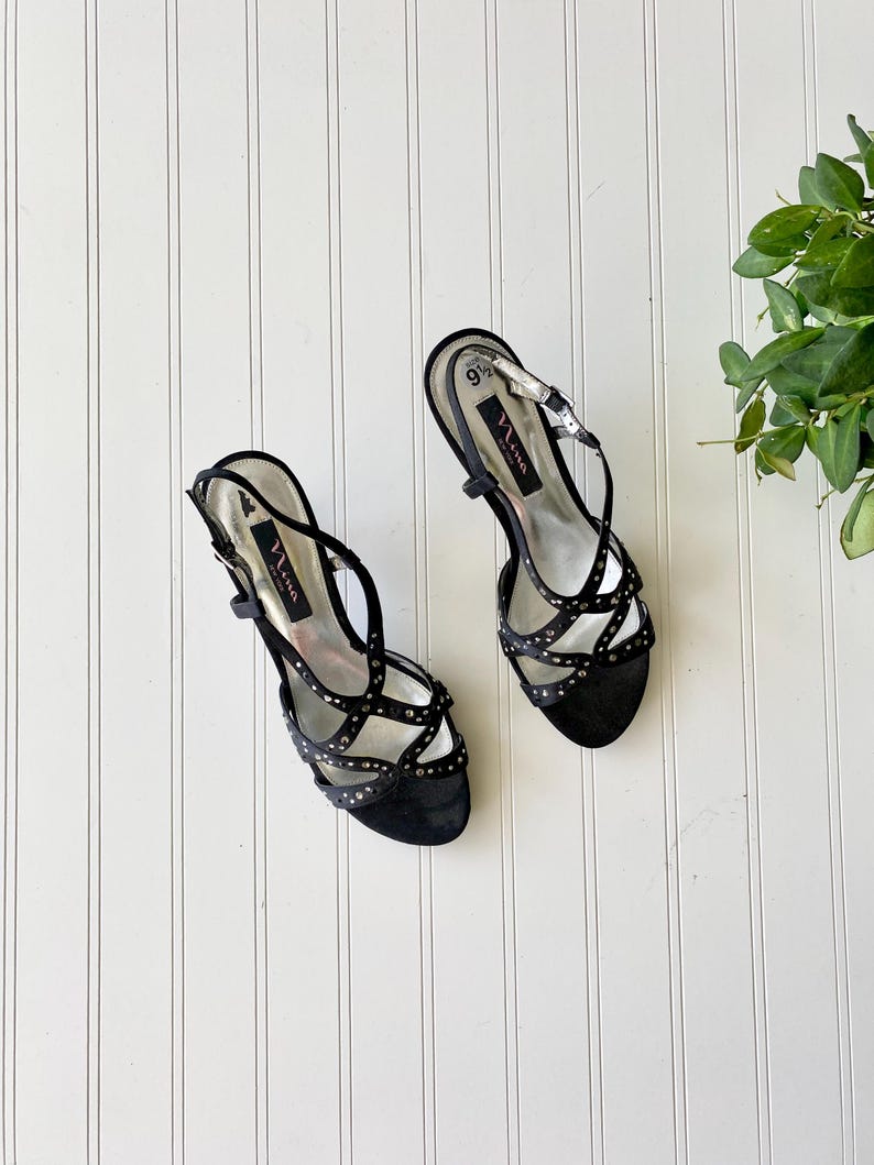 K&ouml;nnte beinhalten: Paar schwarze Sandalen mit hohen Abs&auml;tzen und Riemchen mit silberfarbenen Nieten. Die Sandalen haben einen Slingback-Riemen und einen Schnallenverschluss. Der Markenname "Nina" ist auf der Innensohle sichtbar. Gr&ouml;&szlig;e 9 1/2.