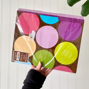 May include: A pack of 12 file folders in a brown base color featuring a pattern of large, colorful circles in shades of pink, light blue, lavender, peach, lime green, and purple. A label on the front reads Hot Chocolate! JACKIE 12 File Folders.