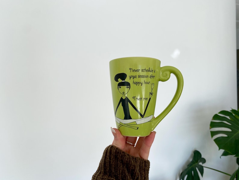 May include: A green ceramic mug with a large handle. The mug features a cartoon illustration of a woman in a yoga pose, with the text "Never schedule a yoga session after happy hour. Trust me."