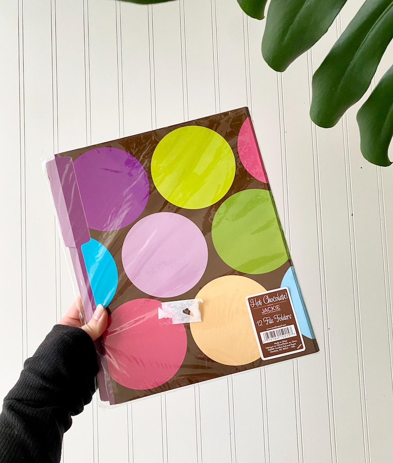 May include: A pack of 12 file folders with a brown background and large, colorful polka dots in shades of lime green, purple, pink, light blue, and peach. A rectangular label on the front reads Hot Chocolate! JACKIE 12 File Folders.