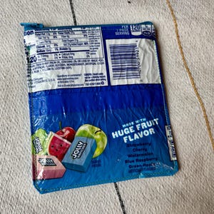 May include: A blue Jolly Rancher candy wrapper, featuring images of fruit and the words "Huge Fruit Flavor." The wrapper lists flavors like strawberry, cherry, and watermelon. Nutritional information is visible on the top left.