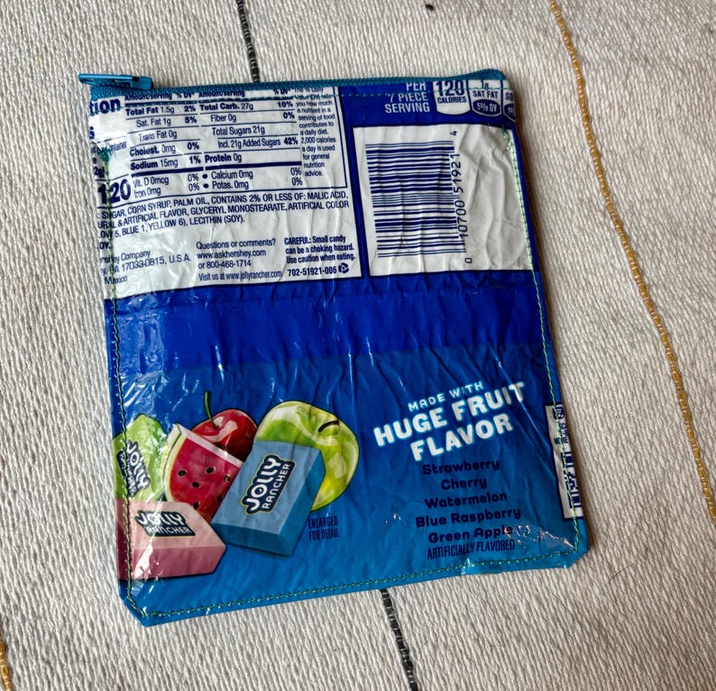 May include: A blue Jolly Rancher candy wrapper, featuring images of fruit and the words "Huge Fruit Flavor." The wrapper lists flavors like strawberry, cherry, and watermelon. Nutritional information is visible on the top left.