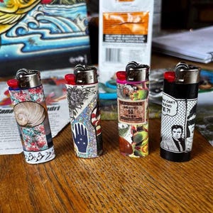 May include: Four decorative lighters with unique designs. One features a seashell, another a hand with a star pattern, a third with a vintage label, and the last with a comic strip design. Each lighter has a red ignition button.