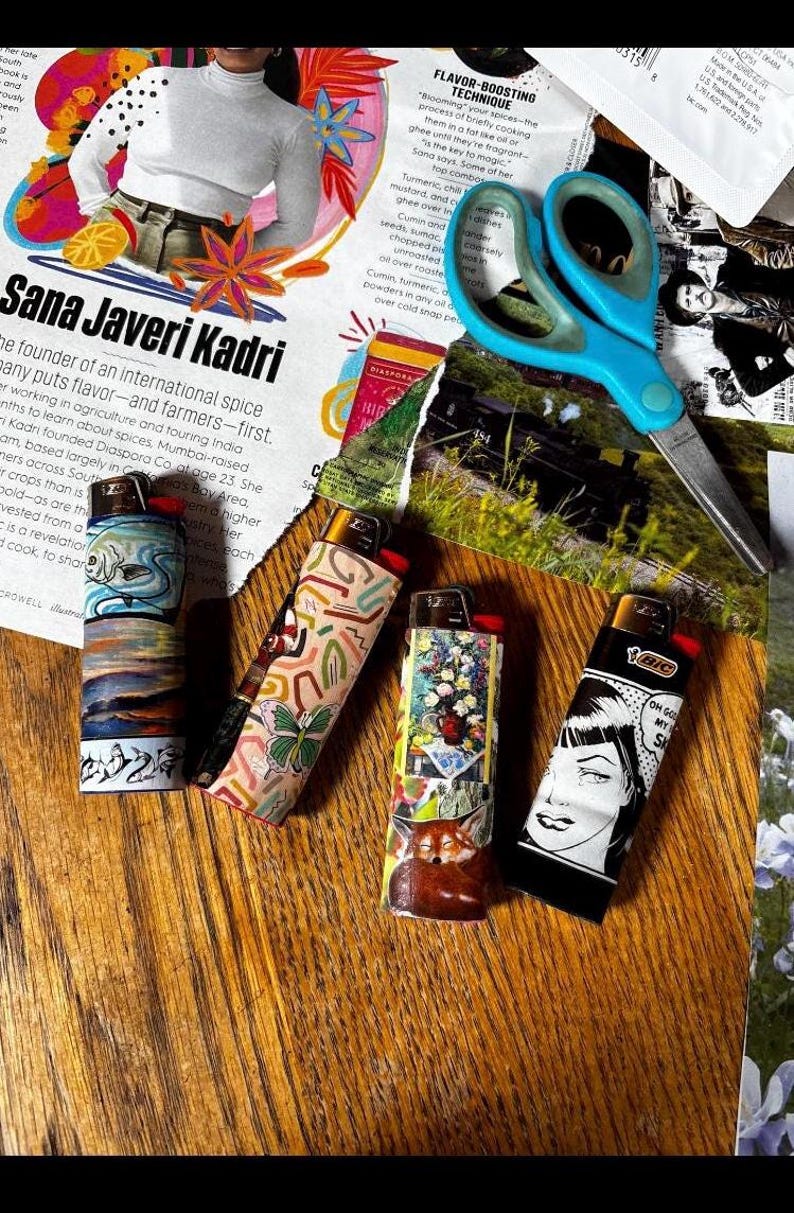 May include: Four BIC lighters with unique designs are displayed on a wooden surface. One features a pop art woman, another a floral arrangement, and the others have abstract patterns. A pair of blue scissors and a magazine are in the background.