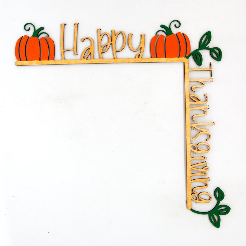 K&ouml;nnte beinhalten: Holz-Dekoration zum Erntedankfest in Eckform. Mit orangefarbenen K&uuml;rbissen, gr&uuml;nen Bl&auml;ttern und den Worten "Happy" und "Thanksgiving" in Schreibschrift. Die Dekoration ist aus hellbraunem Holz gefertigt.