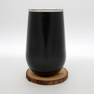 May include: A black stainless steel tumbler with a silver lid, sitting on a wooden coaster.