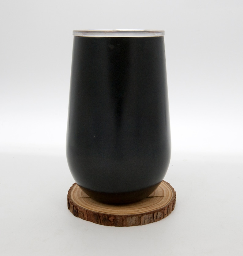 May include: A black stainless steel tumbler with a silver lid, sitting on a wooden coaster.