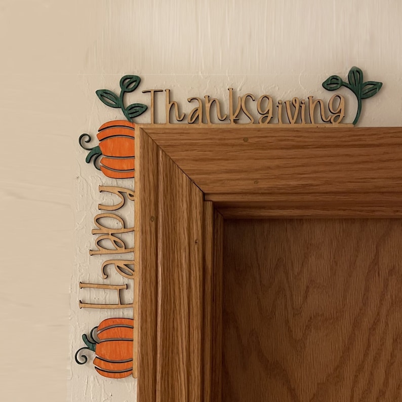 K&ouml;nnte beinhalten: Holz-T&uuml;rdekoration zum Erntedankfest mit den Worten "Happy Thanksgiving" und K&uuml;rbismotiven. Die K&uuml;rbisse sind orange mit gr&uuml;nen Bl&auml;ttern und schwarzen Ranken. Der Text ist in Schreibschrift.