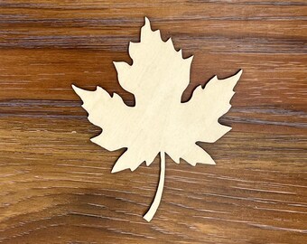 May include: A wooden maple leaf cutout, featuring a detailed design with multiple points. The leaf is light beige in color and rests on a dark brown wooden surface. This decorative item is ideal for fall-themed crafts and home decor projects.