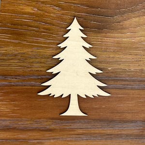 May include: A wooden cutout of a Christmas tree, with a light tan color. The tree is set against a brown wooden background. The tree has a detailed design with multiple layers of branches, perfect for holiday crafts and decorations.