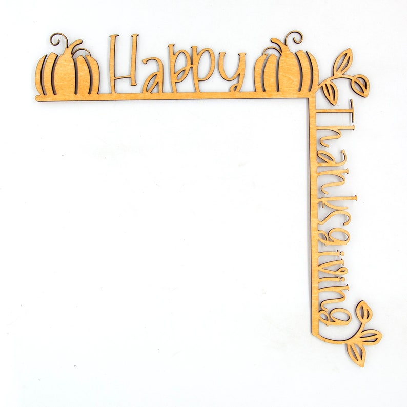 K&ouml;nnte beinhalten: Eckdekoration aus Holz mit den Worten "Happy Thanksgiving" ausgeschnitten. Das Design umfasst zwei K&uuml;rbisse und Bl&auml;tterakzente. Das Holzst&uuml;ck ist hellbraun und liegt auf einem wei&szlig;en Hintergrund.