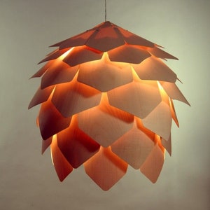 May include: A wooden pendant light fixture shaped like a pine cone with a warm, orange glow. The light is made of many individual pieces of wood that are layered together to create the shape of a pine cone.