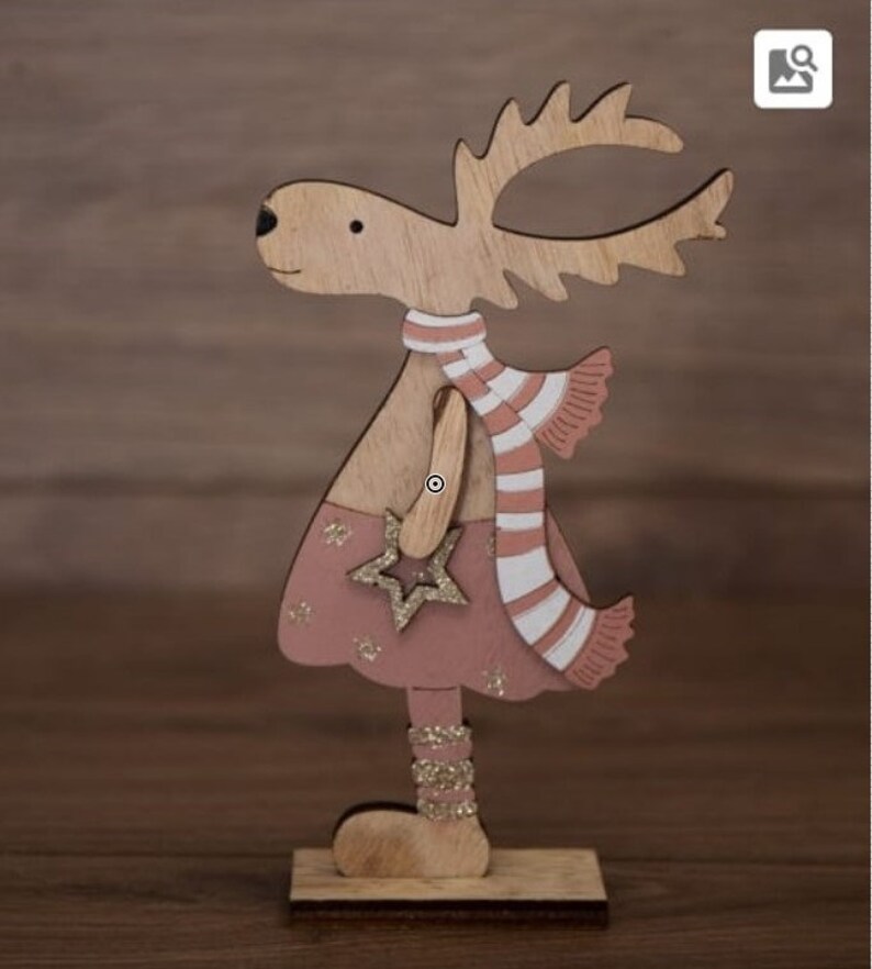 Op de afbeelding: Een houten rendierfiguur met een roze jurk, een wit-roze gestreepte sjaal en een gouden ster. Het rendier staat op een houten voet.