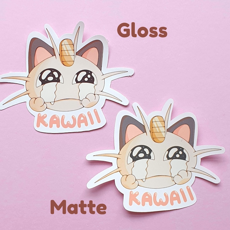 May include: Two stickers featuring a cartoon cat with a sad expression and the word "KAWAII". One sticker has a glossy finish, and the other has a matte finish. The cat is primarily beige with brown and tan accents.