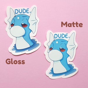 May include: Two stickers featuring a cartoon blue sea creature with red eyes and the word "DUDE." above its head. One sticker is labeled "Gloss" and the other "Matte."