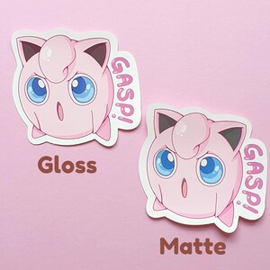 May include: Two stickers featuring a pink cartoon character with large blue eyes and the word "GASP!" in pink. One sticker is labeled "Gloss" and the other "Matte". The background is a solid light pink.