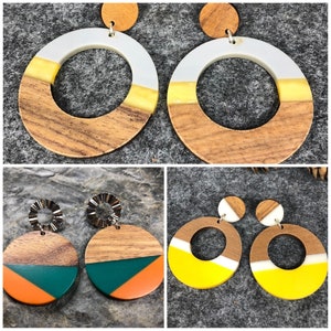 Può includere: Quattro paia di orecchini rotondi in legno con intarsi in resina di diversi colori. Gli orecchini sono in due stili, uno con un intarsio bianco e giallo e l'altro con un intarsio verde e arancione.