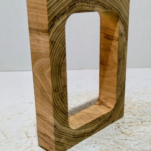 Op de afbeelding: Een rechthoekig houten blok met een rechthoekige uitsparing. De houtnerf is zichtbaar, wat de natuurlijke textuur en kleurvariaties van het materiaal laat zien. Het object heeft een natuurlijke bruine kleur.
