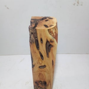 Könnte beinhalten: Ein natürlicher Holzblock mit einer rauen, unregelmäßigen Oberfläche und verschiedenen Knoten und Maserungen. Das Holz ist hellbraun mit dunkleren braunen Streifen.