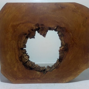 Könnte beinhalten: Ein großes, unregelmäßig geformtes Stück Holz mit einem runden Loch in der Mitte. Das Holz ist hellbraun und hat eine natürliche, rustikale Oberfläche.