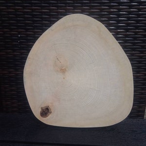 Könnte beinhalten: Eine helle Holzscheibe mit einer natürlichen, unregelmäßigen Form und einem Knoten an der Unterseite. Das Holz hat eine hellbraune Farbe und eine glatte Oberfläche.