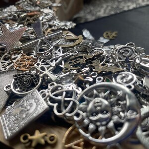 May include: A large pile of silver charm pendants with various designs, including stars, moons, crosses, and other symbols. The charms are perfect for jewelry making or crafting.