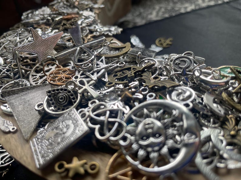May include: A large pile of silver charm pendants with various designs, including stars, moons, crosses, and other symbols. The charms are perfect for jewelry making or crafting.