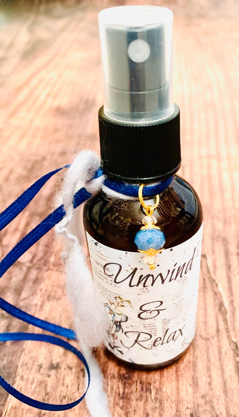 May include: A small brown glass bottle with a black spray top and a blue and gold charm. The bottle is labelled "Unwind & Relax".