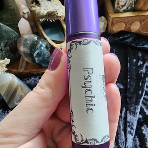 May include: A purple roller bottle with a white label that says "Psychic". The bottle is being held in a hand.