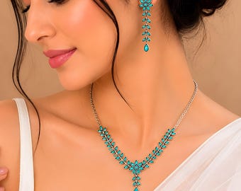May include: A silver-toned jewelry set featuring a necklace and earrings. The necklace and earrings have a floral and leaf design with turquoise-colored stones. The earrings are long and dangle, while the necklace sits on the collarbone.