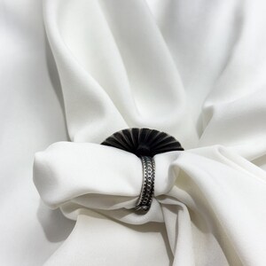 May include: A silver ring with a decorative, fan-shaped design. The ring is made of metal and has a textured surface.