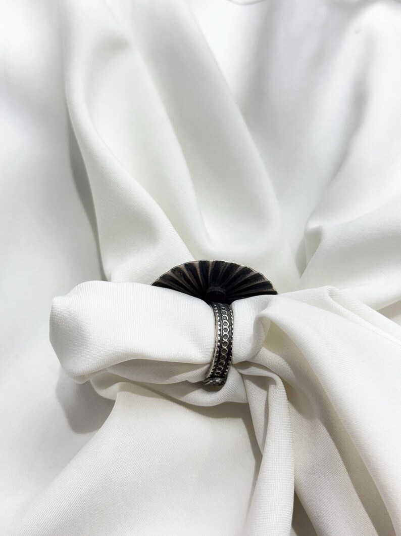 May include: A silver ring with a decorative, fan-shaped design. The ring is made of metal and has a textured surface.