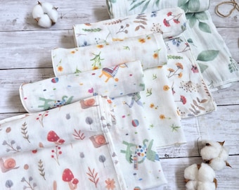 May include: A collection of rolled muslin swaddle blankets featuring various patterns including green eucalyptus leaves, colorful wildflowers, small snails, red mushrooms, and whimsical animal illustrations on a white background with cotton bolls.