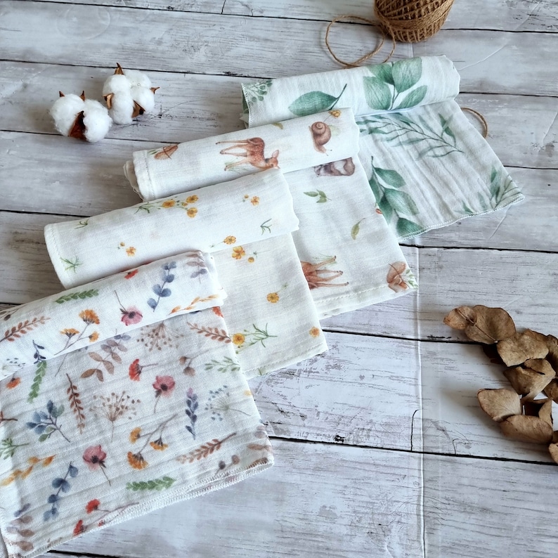 Pu&ograve; includere: Quattro bavaglini in mussola bianca per neonati con diverse stampe floreali e a tema natura. Le stampe includono un cervo, una lumaca, foglie e fiori.