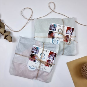 Pu&ograve; includere: Due pacchi avvolti in carta velina bianca e legati con spago. Ogni pacco ha una piccola carta allegata con il testo "The softest made materials for babies & children" e un logo che dice "NINKI NANKA".