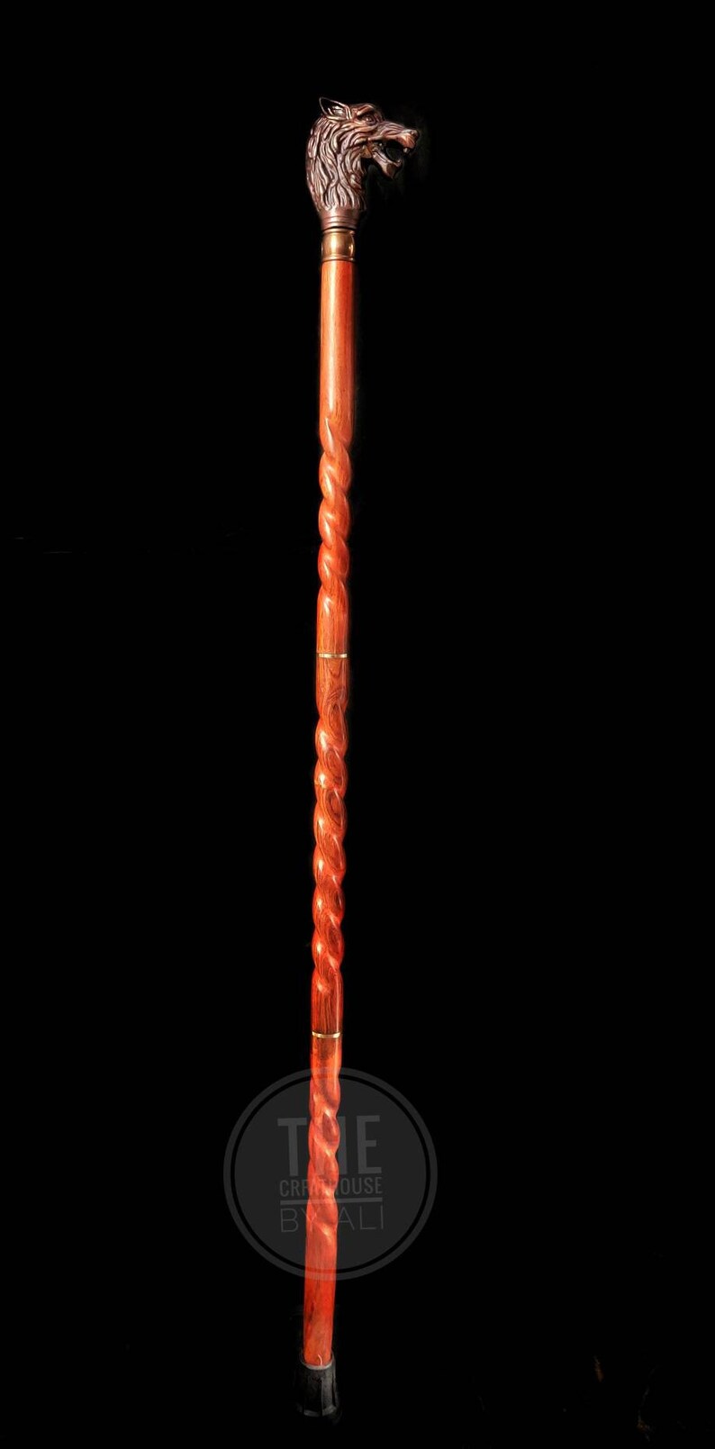 Pode incluir: Uma bengala de madeira com uma pega em forma de cabe&ccedil;a de lobo. A bengala &eacute; de cor castanho-avermelhada e tem um design torcido. A cabe&ccedil;a de lobo &eacute; feita de metal e tem um acabamento dourado.
