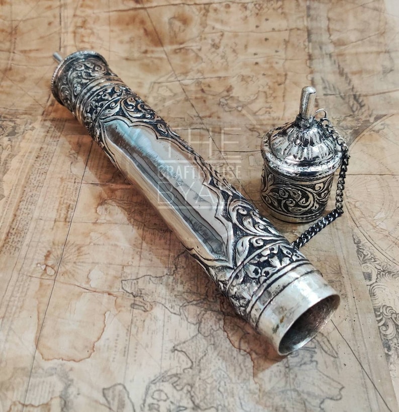 Pu&ograve; includere: Astuccio per rotolo argentato ornato e contenitore abbinato con intricati motivi floreali e geometrici. L'astuccio cilindrico &egrave; lungo, con un tappo decorativo. Il contenitore &egrave; piccolo, con un coperchio attaccato da una catena. Su una mappa.