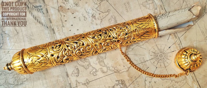 May include: A gold metal scroll tube with intricate floral designs. The tube has a chain attached to a decorative cap. The tube is open and a rolled piece of paper is partially visible.